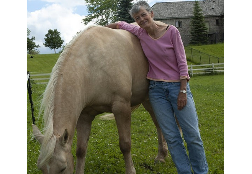 Shannon Bruce with horse in a green field. A farmhouse is in the background.