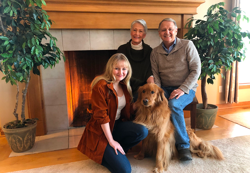 Shannon family of four with their golden retriever posing by a lit fireplace in a living room.