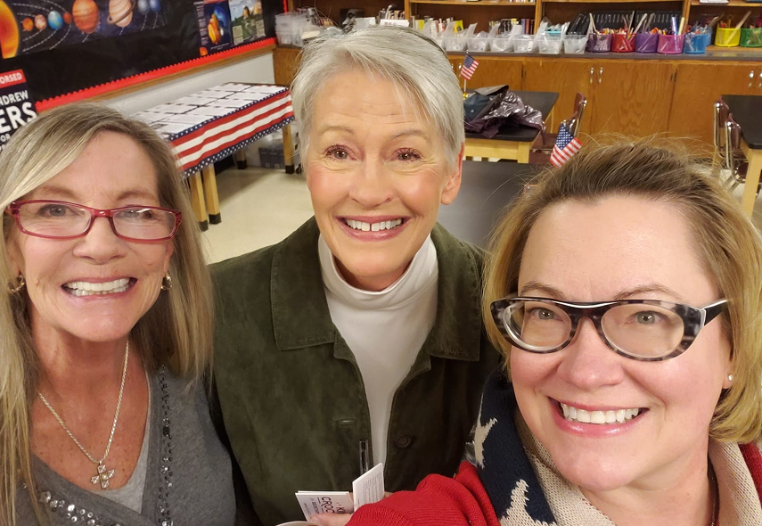 Shannon Bruce take a cheerful selfie in a classroom, with space-themed posters and American flags in the background.