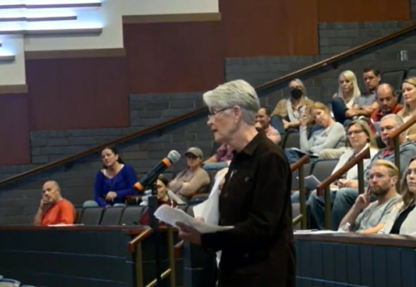 Shannon Bruce speaks, reading from papers, in a lecture hall while the audience sits in tiered seating behind her.
